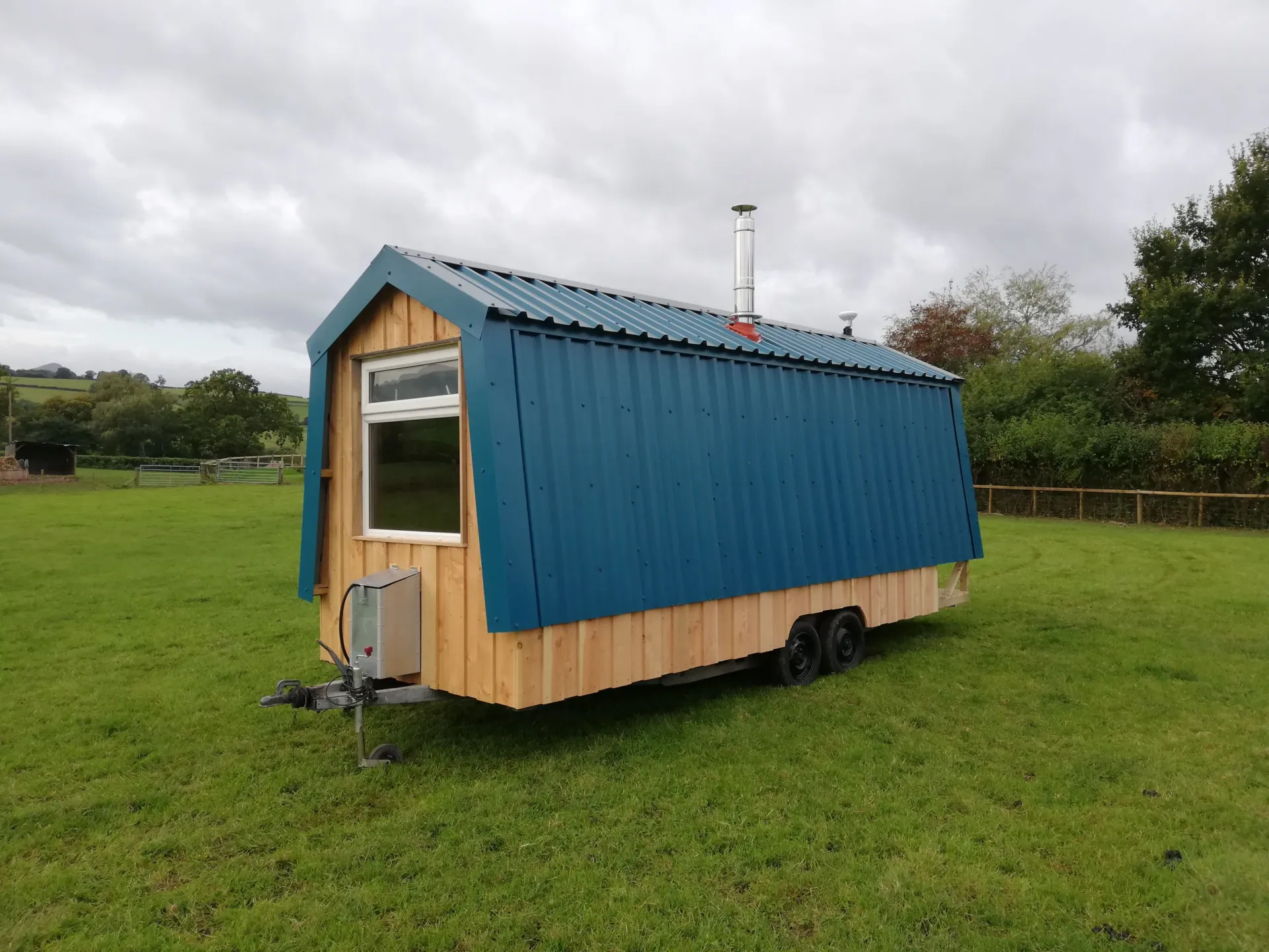 A blue and wooden trailer is parked in a grassy field.