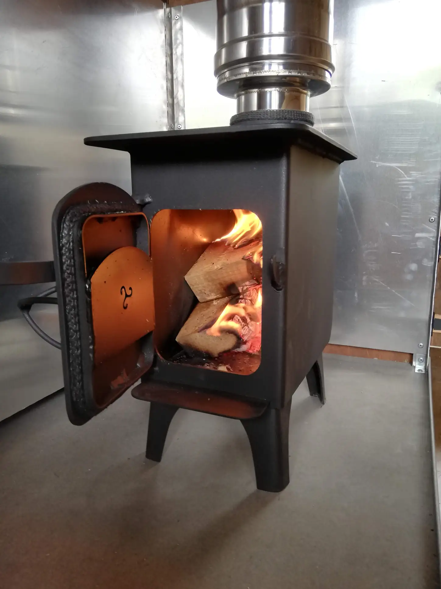 A wood stove with the door open and a chimney coming out of it.