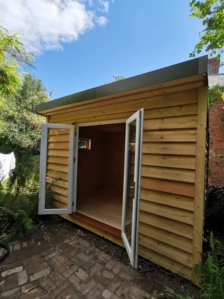 A wooden shed with white doors is sitting on top of a brick patio.