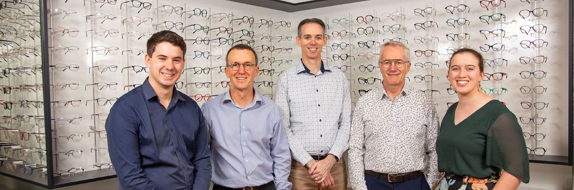 A group of people are posing for a picture in front of a display of glasses for purchase.
