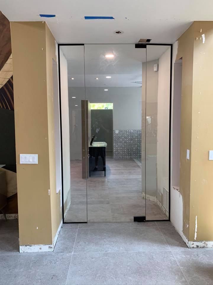 Glass door with black framing between tan walls, leading to a room with gray flooring.