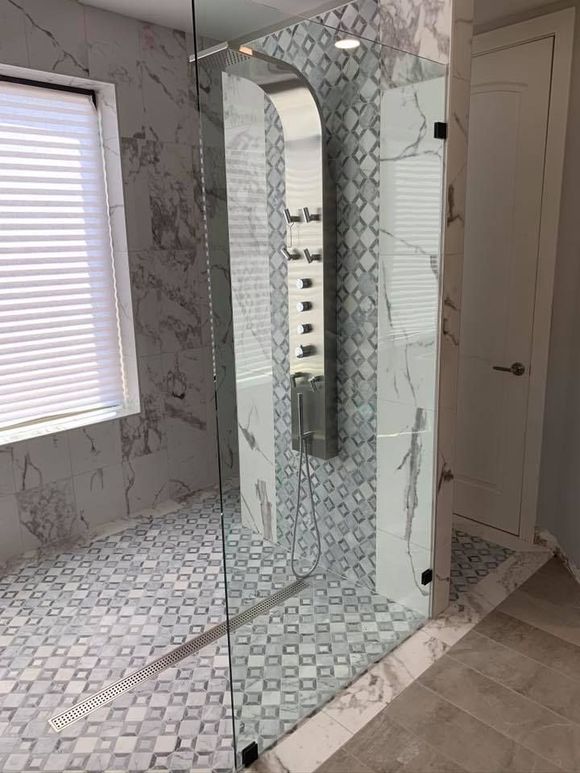 Modern bathroom with a glass shower, marble tiles, and patterned floor.
