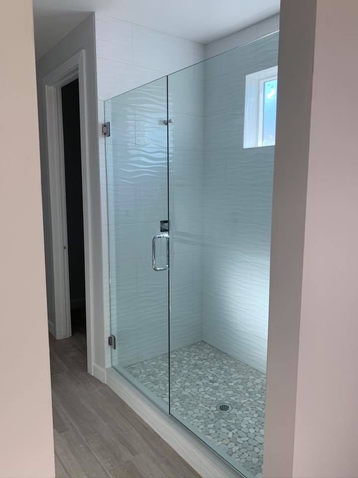 Glass shower enclosure in a bathroom with pebble flooring and textured white wall tiles.