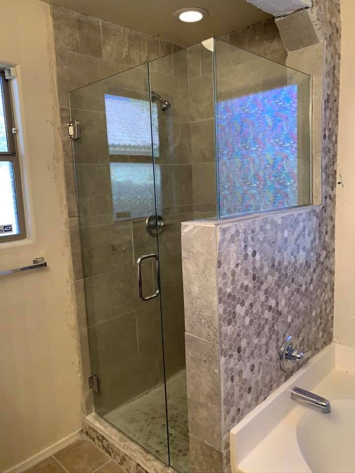 A glass shower enclosure with tile walls and a door; adjacent to a tub.