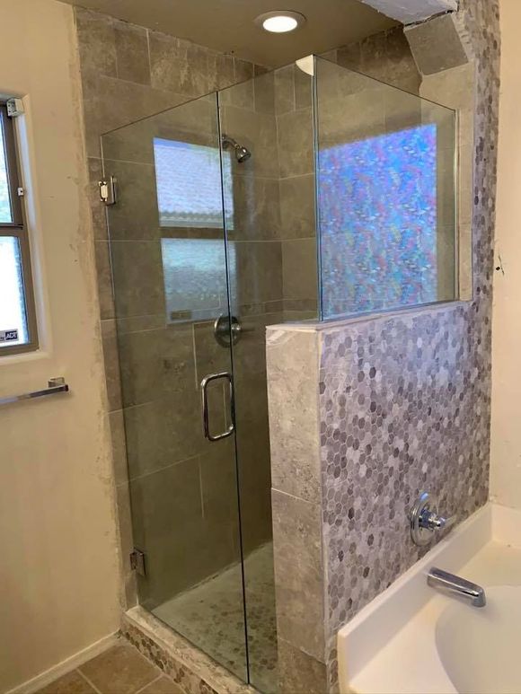 Glass shower enclosure with tiled walls and a window, next to a bathtub.