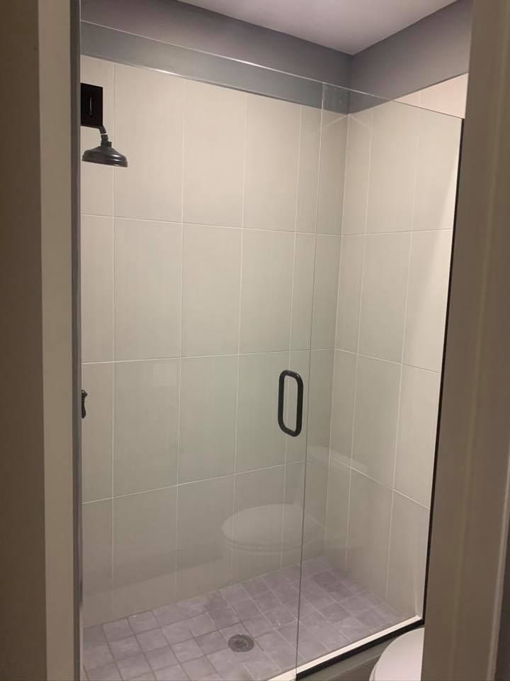 Shower with clear glass door, gray tiled walls and floor, dark shower head and door handle.