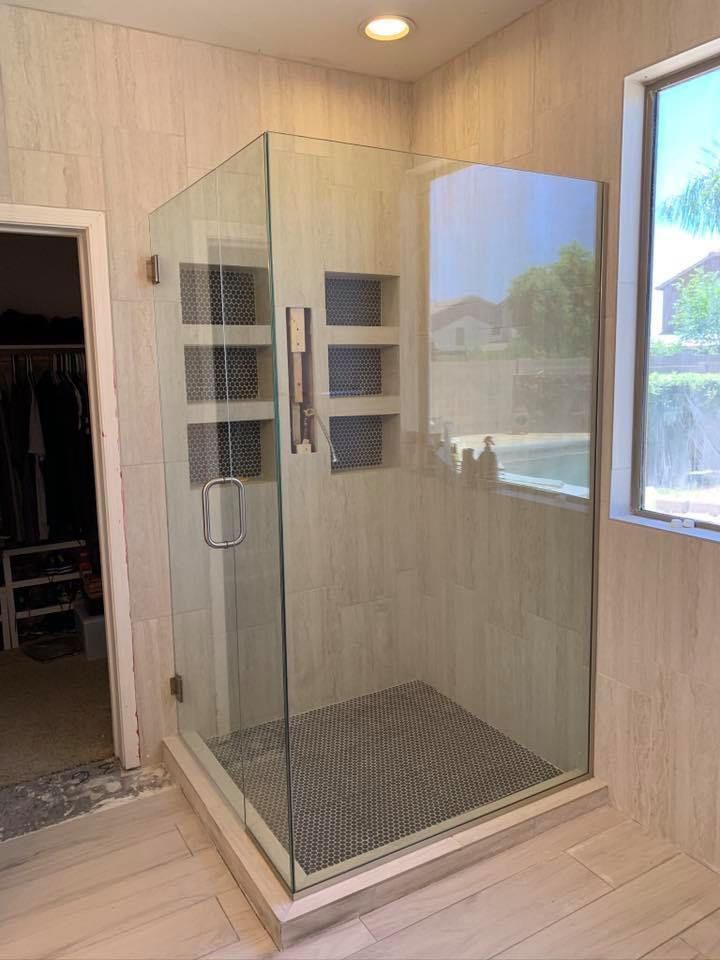 Glass shower with tiled walls and floor, built-in shelving, next to a window, and an open closet.