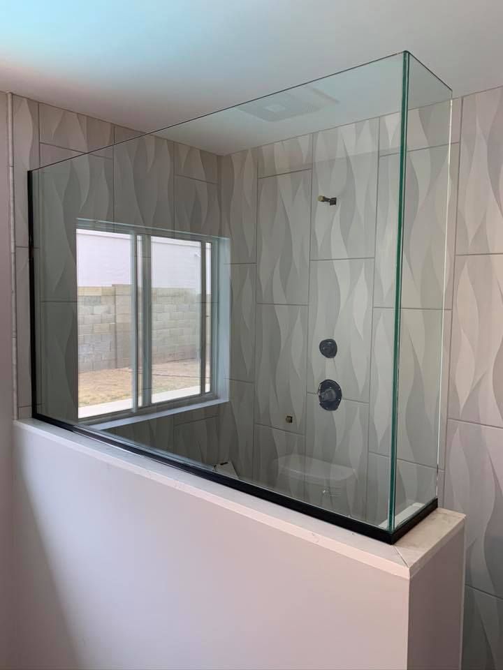 Glass-enclosed shower on a half wall with a window view and wavy gray tile.