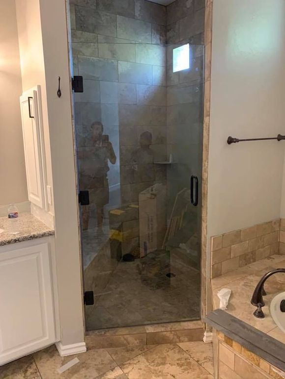 A clear glass shower door with black hardware in a beige bathroom.
