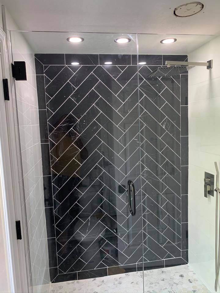 Dark gray herringbone tile shower with glass door, black fixtures, and recessed lighting.