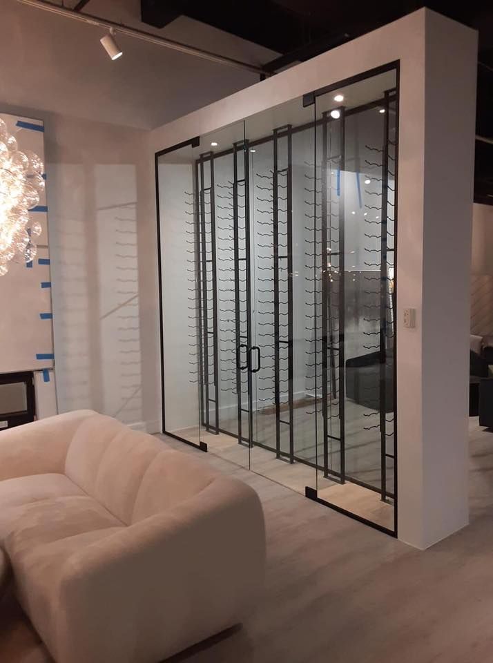 Modern wine cellar with glass doors and black metal framing, next to a white sofa.