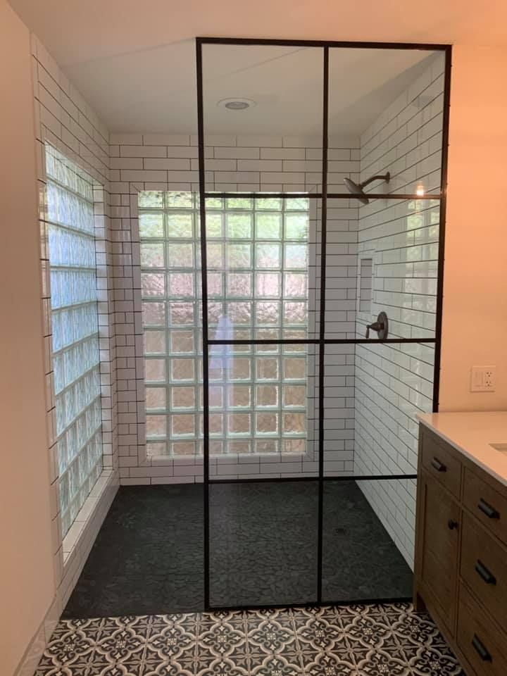 Shower with black-framed glass door, white subway tile, glass block window, dark floor, and a dark vanity.