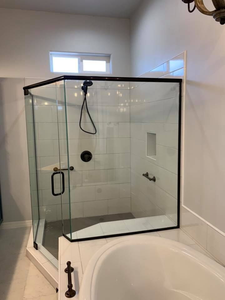 Black-framed glass shower with a black showerhead and hardware, built into a white-tiled bathroom.