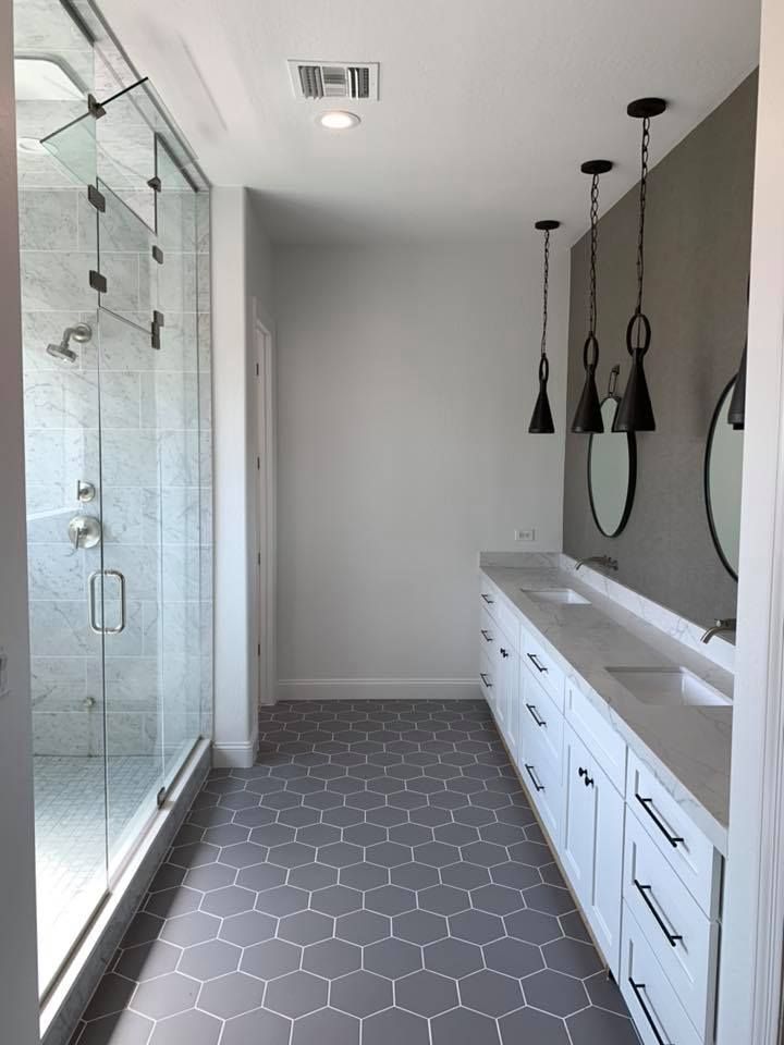 Modern bathroom with gray hexagon tile floor, white vanity, and glass shower.