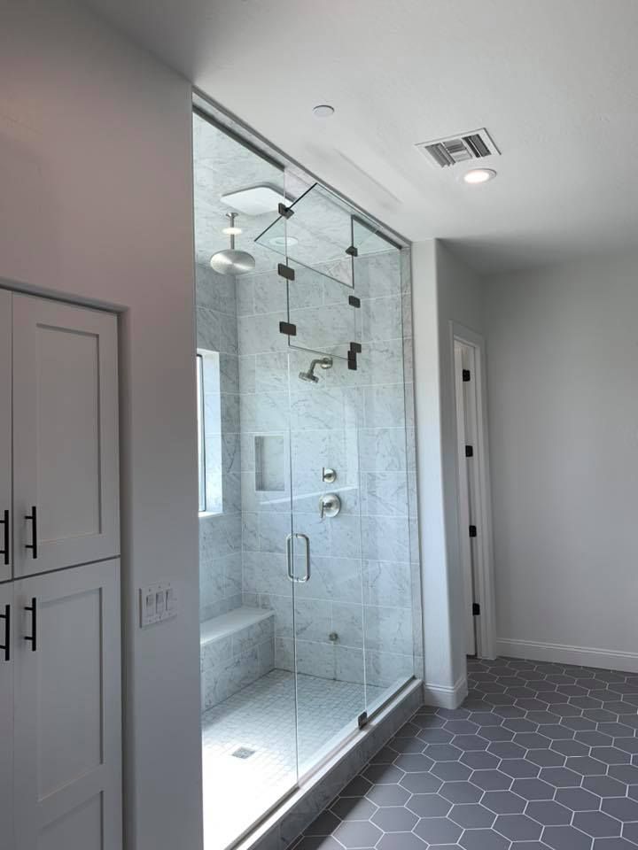 Modern shower with glass door, white tiled walls, built-in bench, and a gray hexagonal tiled floor.