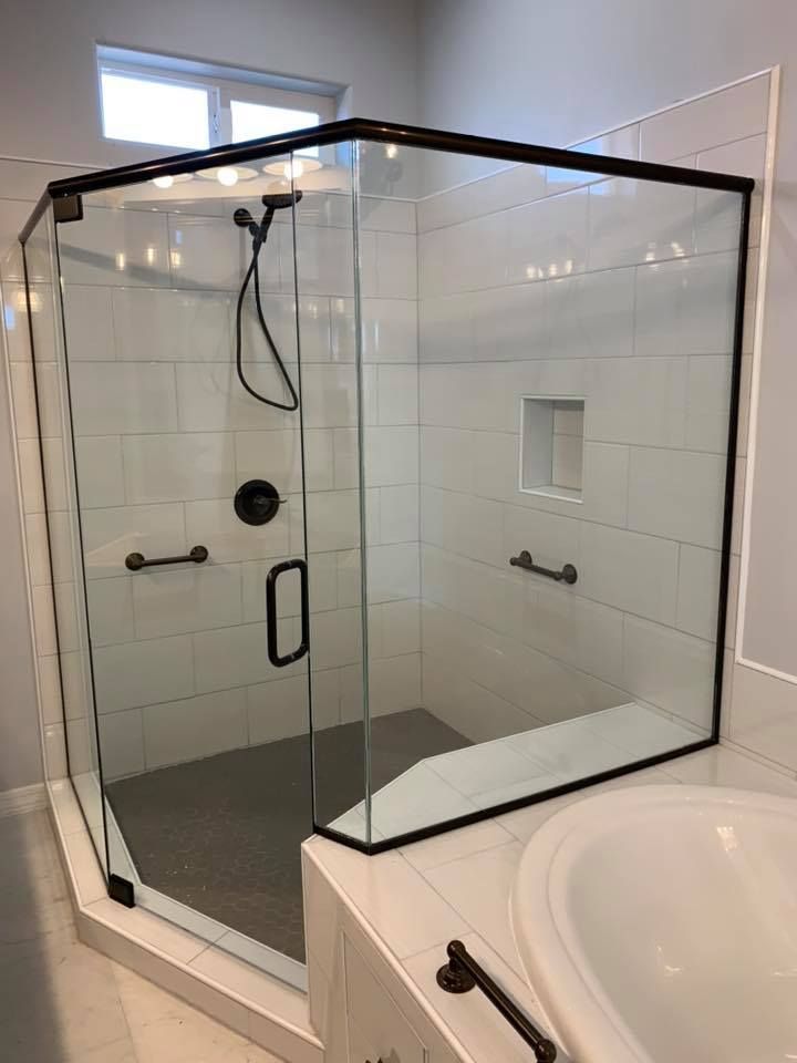 Modern shower with black frame, clear glass, white tile walls, and dark fixtures. Includes grab bars.