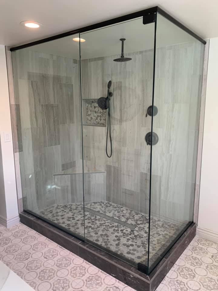 Frameless glass shower with black fixtures and pebble tile floor.