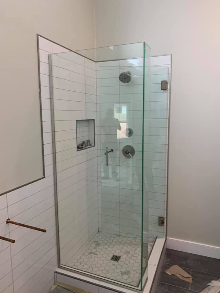 Glass shower enclosure with white tile and chrome fixtures.