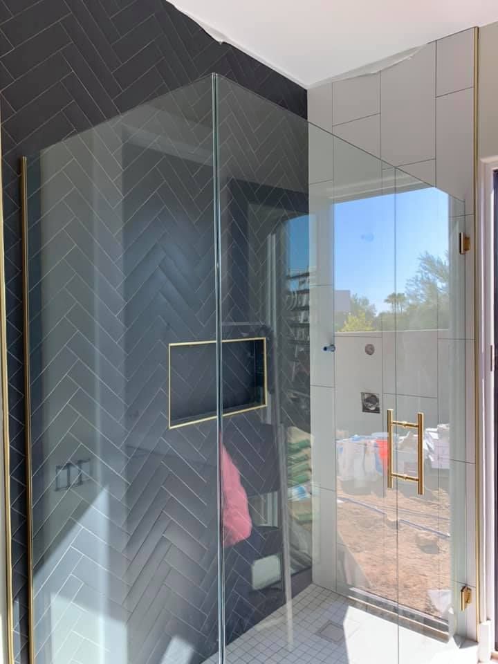 Corner shower with dark gray herringbone tile and glass doors, gold hardware.