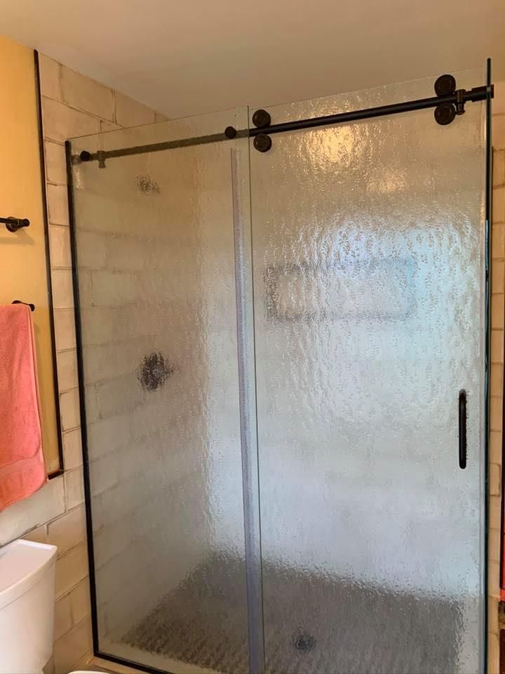 Shower with textured glass doors, black hardware, and stone-look tile.