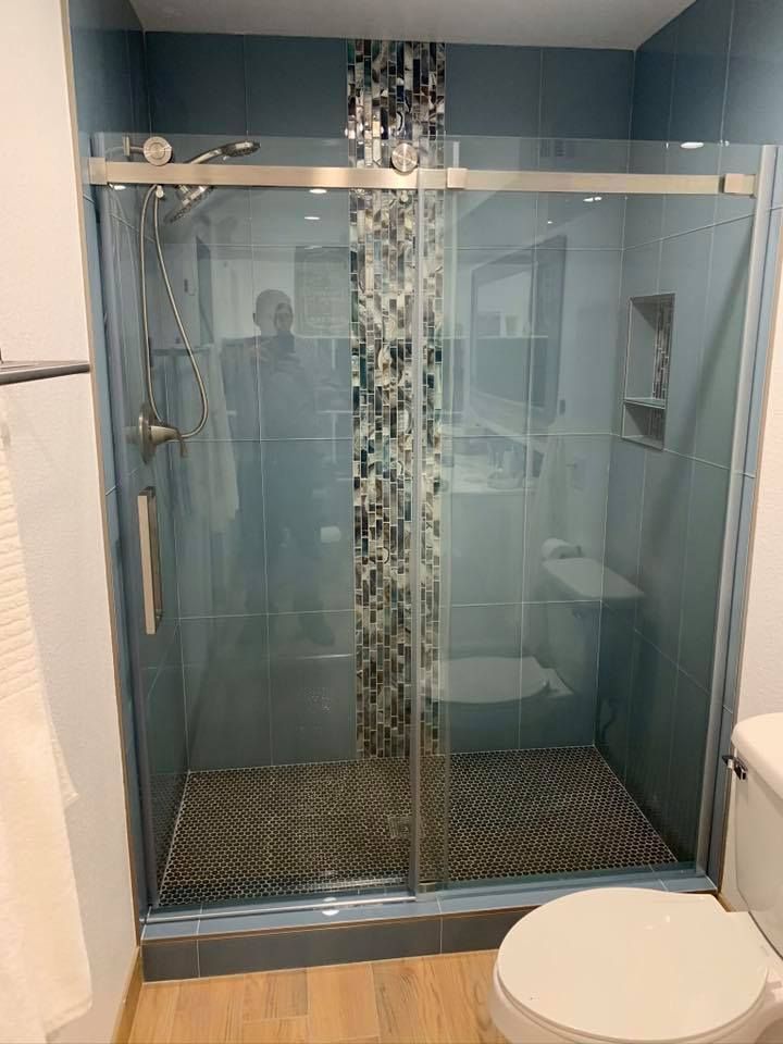 Shower with glass doors, blue tile walls, mosaic accent, and a toilet in front.
