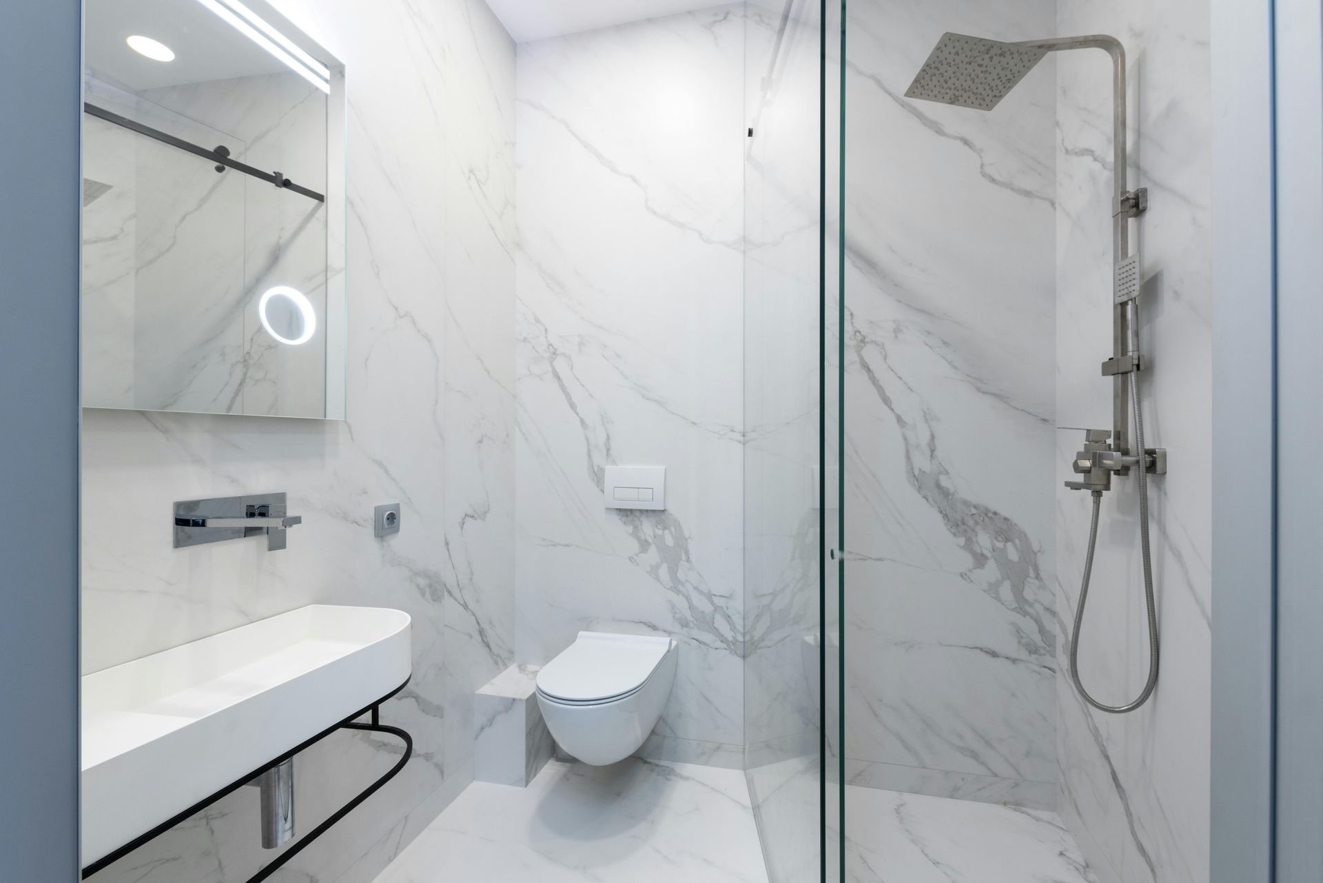 Modern white bathroom with marble tile walls, glass shower, and floating sink.