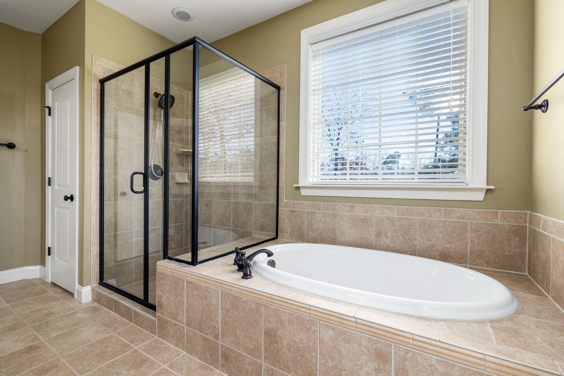 A modern bathroom featuring a beige tiled soaking tub next to a glass-enclosed shower with black frames.