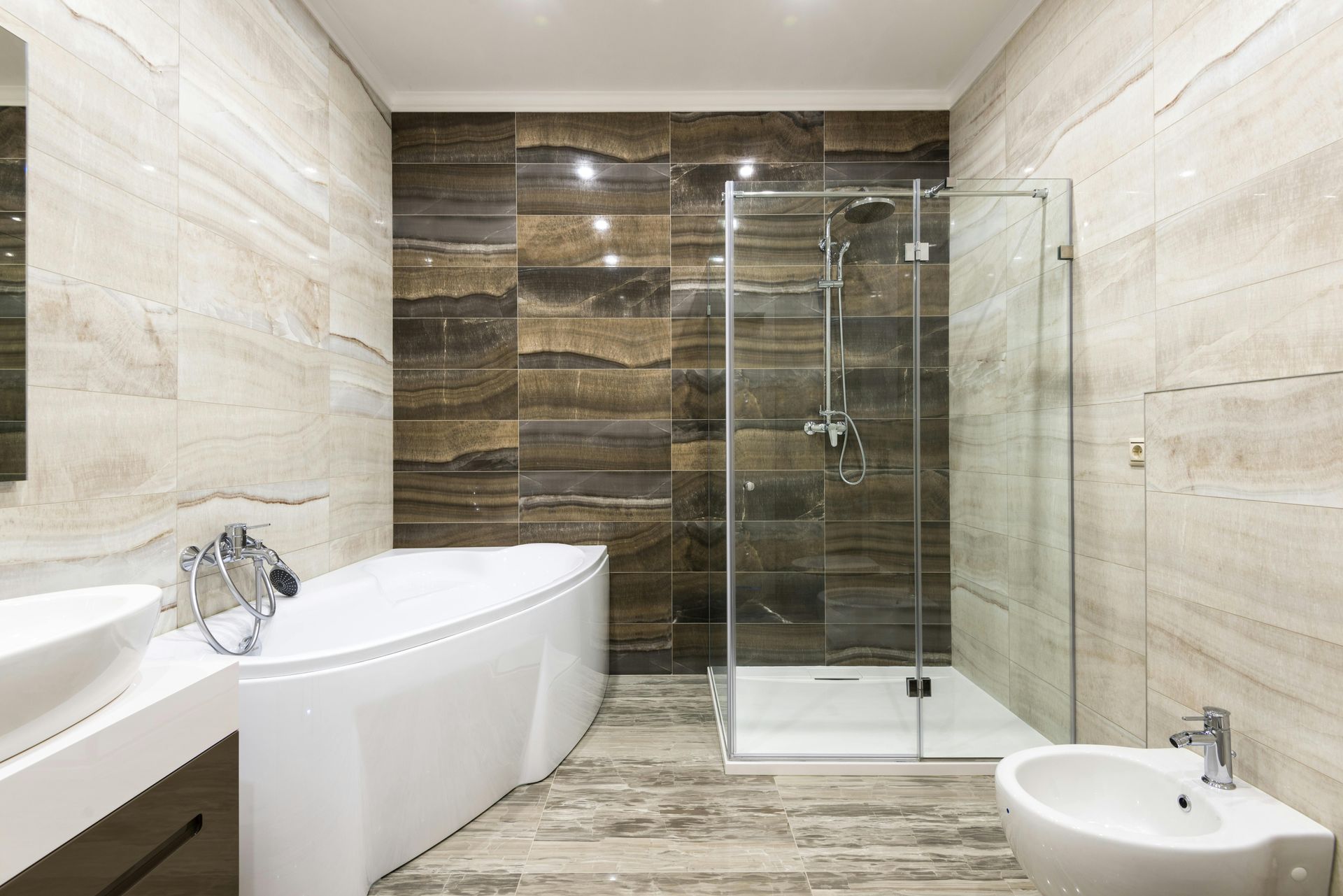 Modern bathroom with white tub, glass shower, and brown and beige tile.