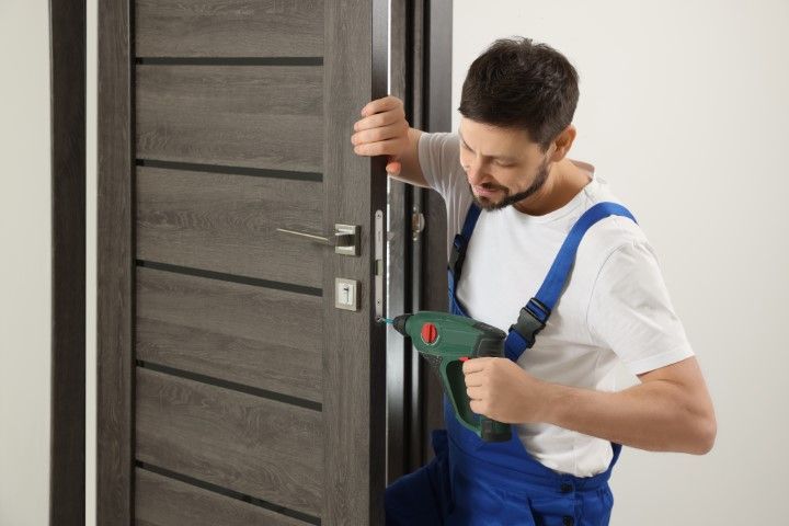 A man in a blue jumper is using a drill to install the door knob properly.