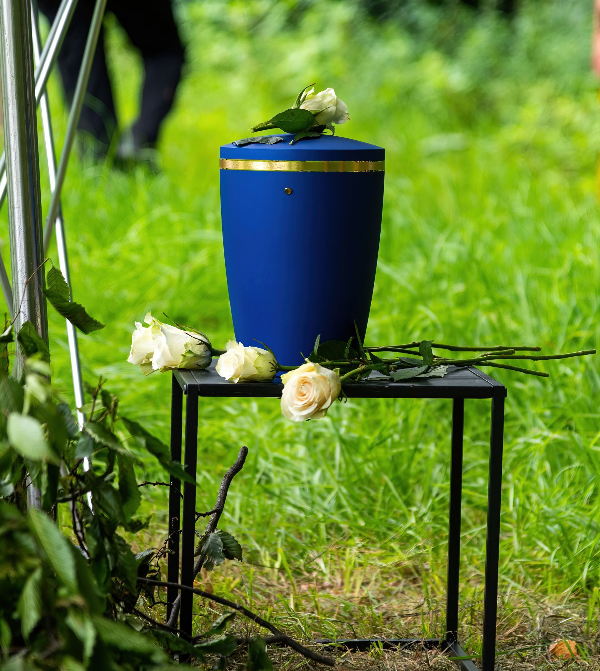 A blue cremation urn on top of a platform, witn flowers in front.