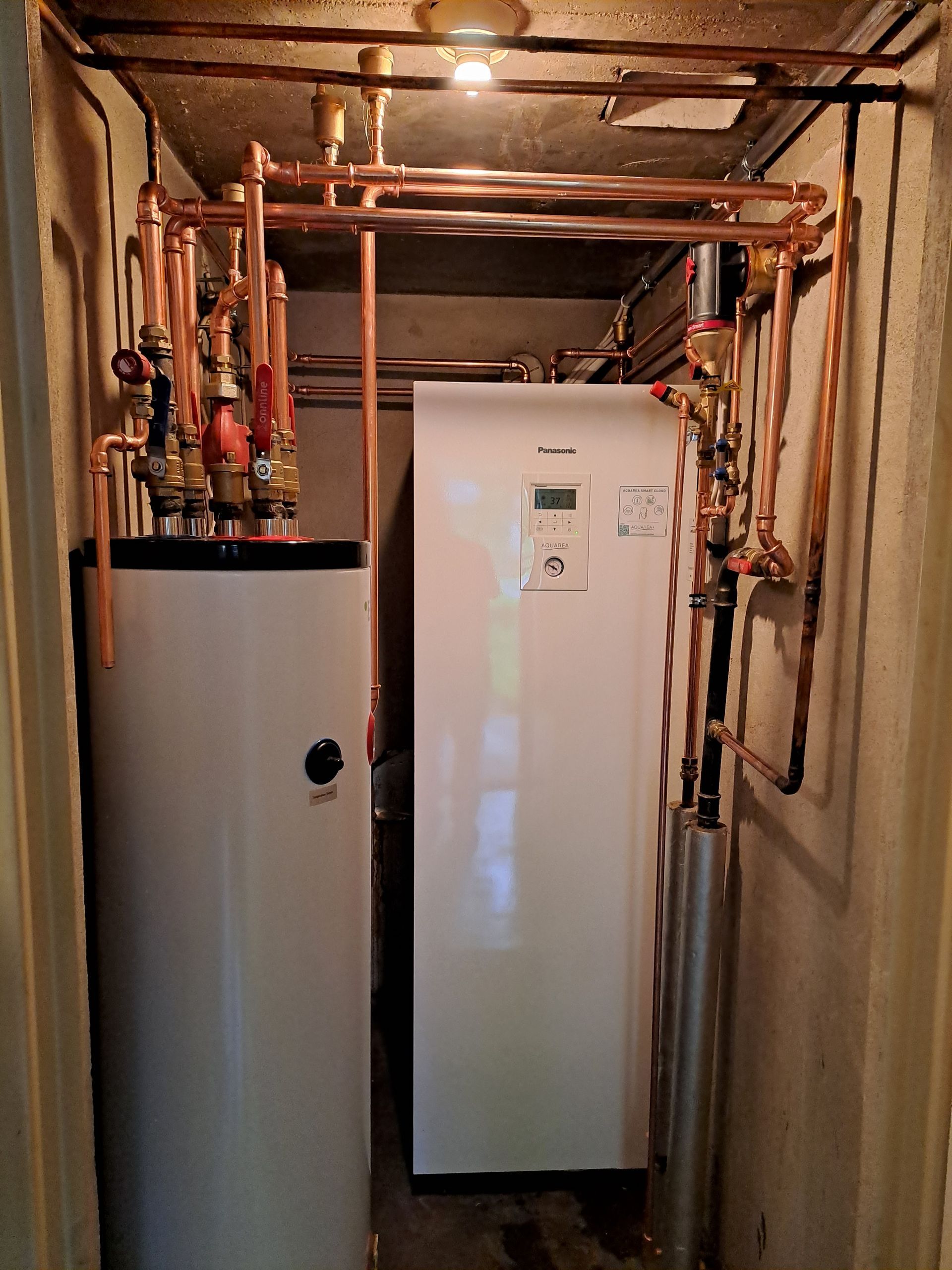 Valkoinen vedenlämmitin on huoneessa, jossa on kupariputket.