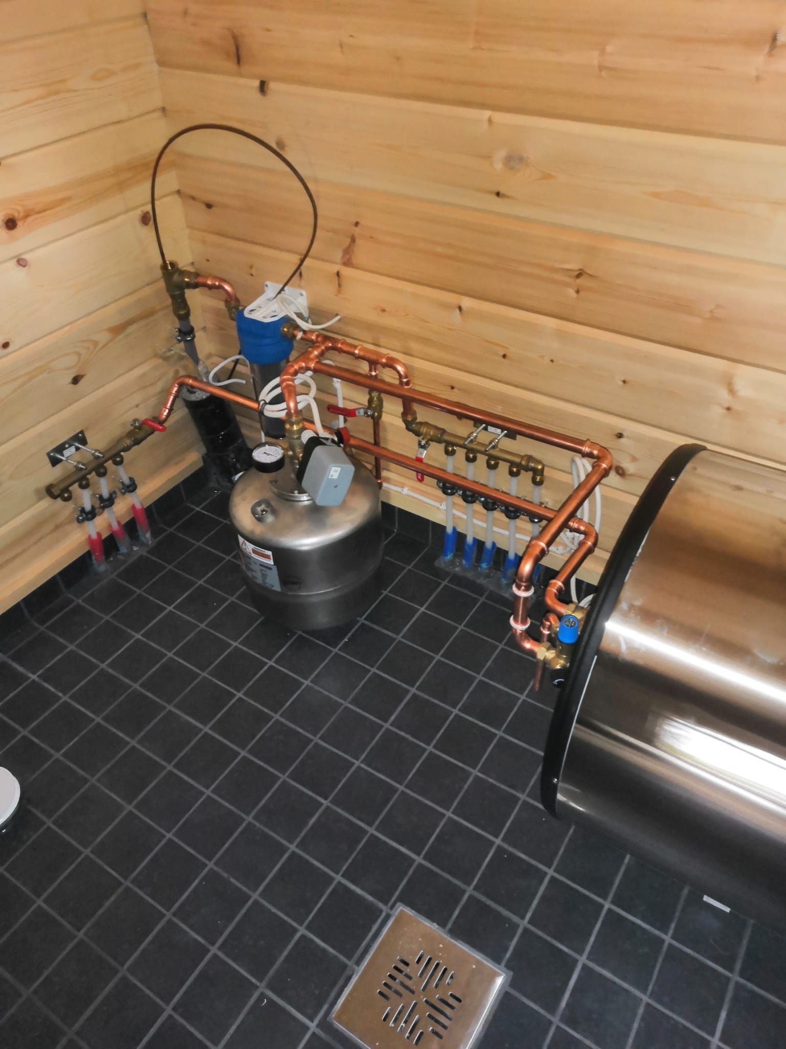 Huone, jossa on ruostumattomasta teräksestä valmistettu säiliö ja kupariputket lattialla.