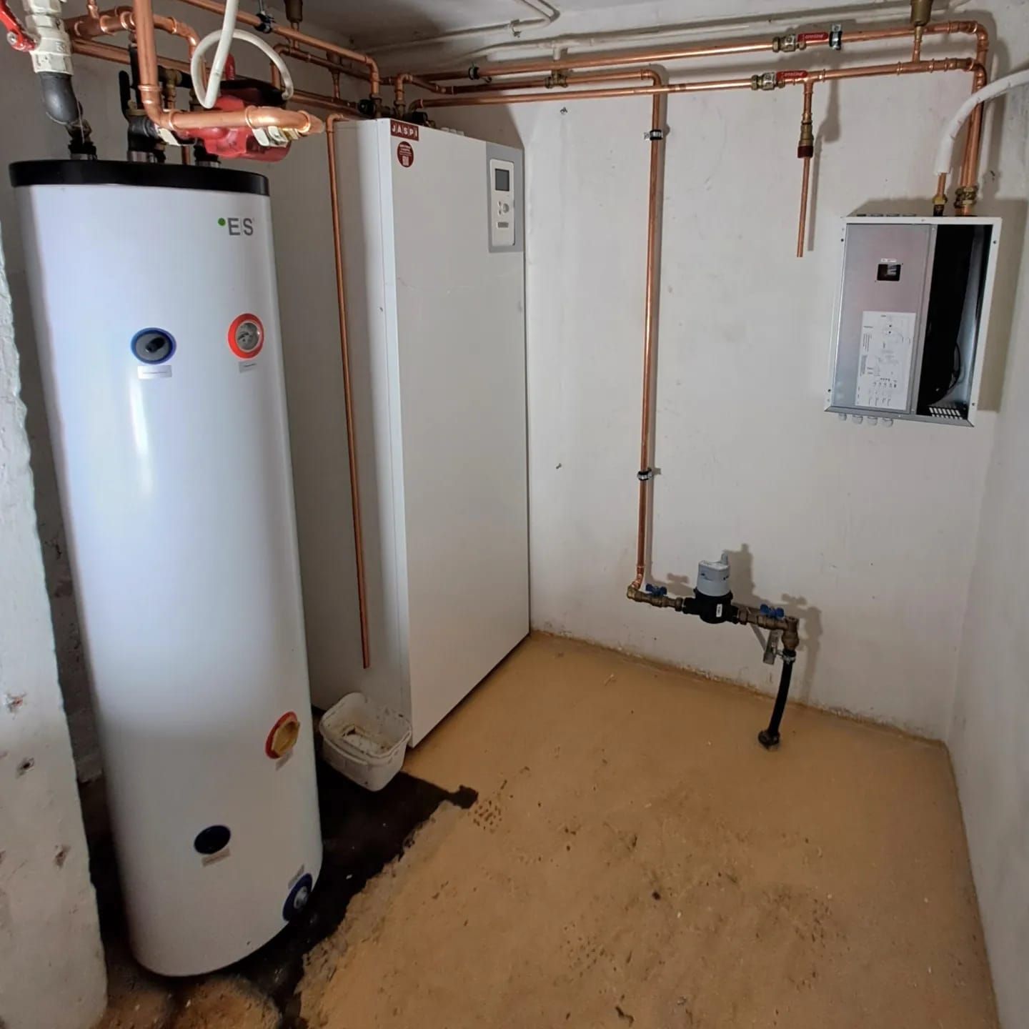 Huone, jossa on valkoinen vedenlämmitin ja kupariputket.