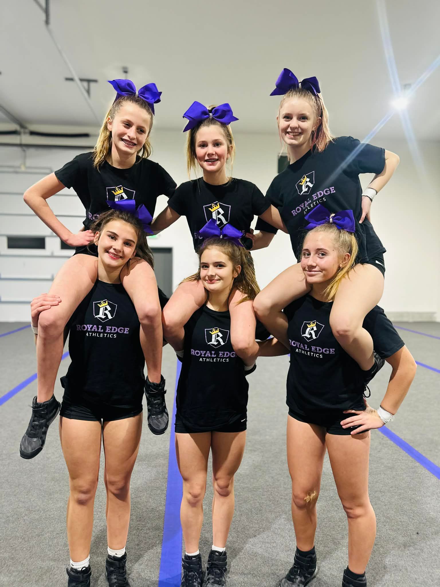 Cheerleaders in blue uniforms performing a three-level pyramid indoors on a blue mat.