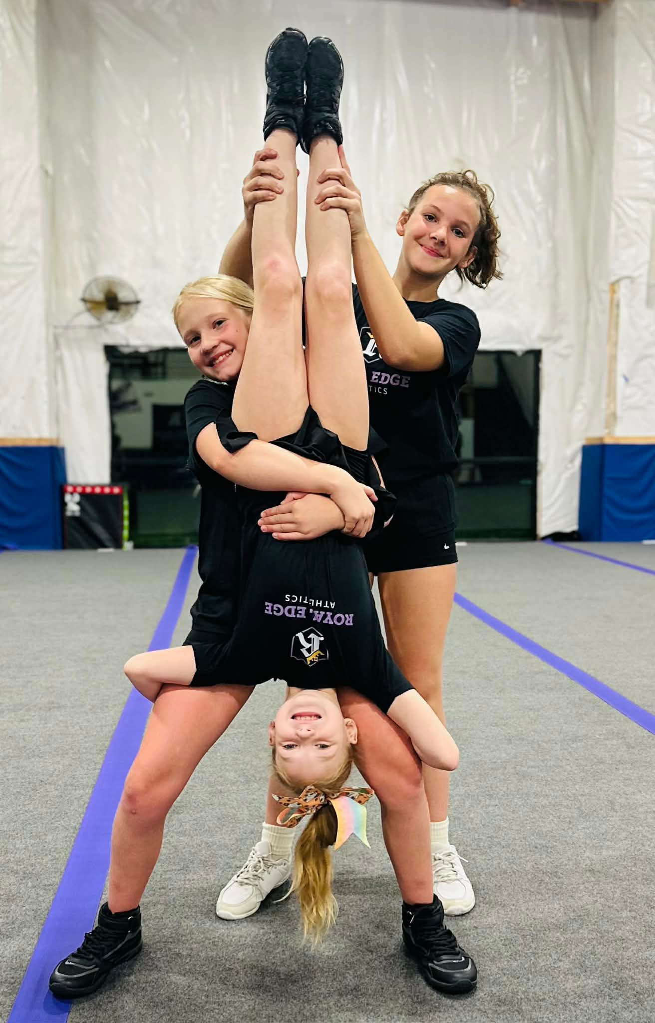 Girl stretching her leg while smiling in a gym setting, with exercise balls and mat.