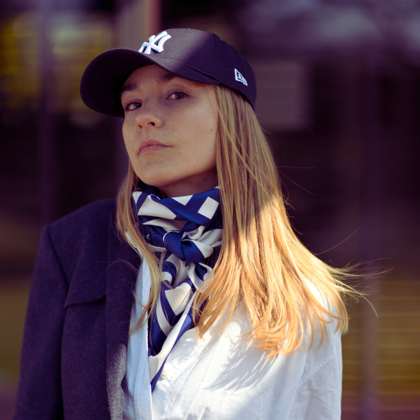 A model in a cap wearing a large blue and cream silk scarf