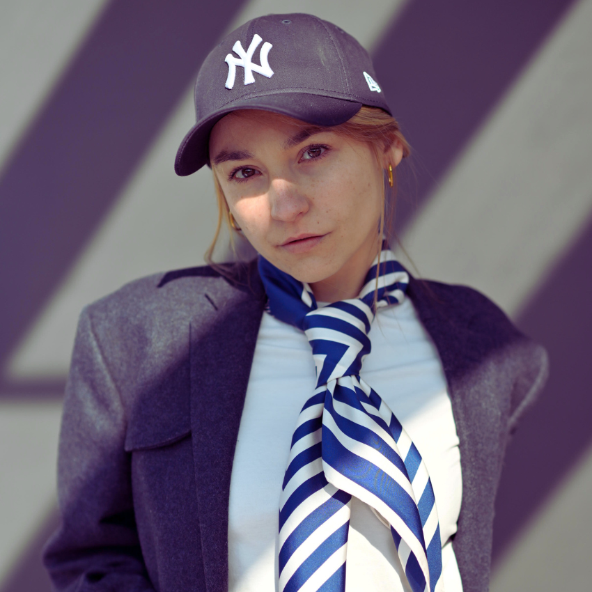 A model in a cap wearing a large blue and cream silk scarf