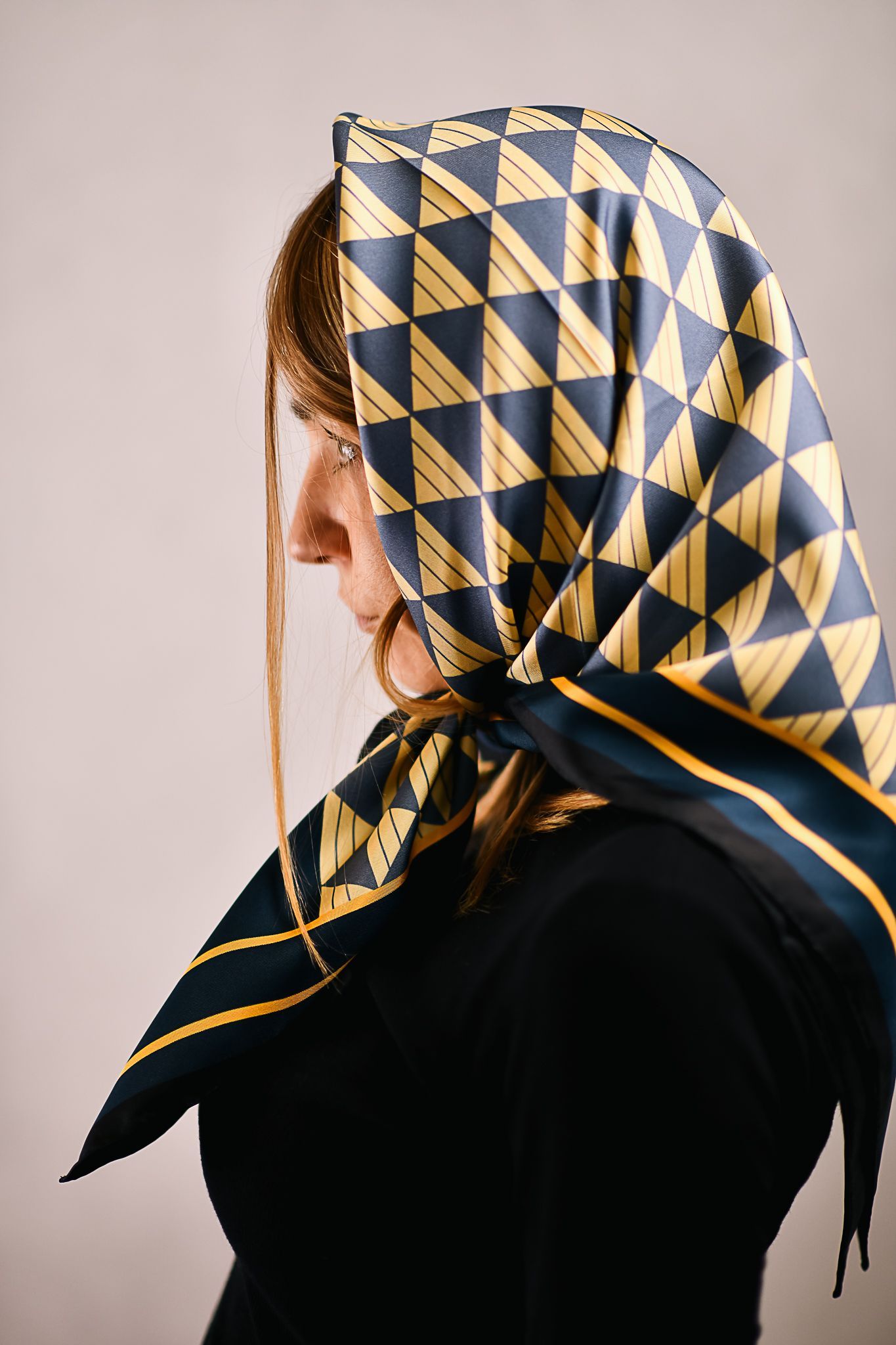 A model wearing an elegant art deco mulberry silk scarf for women, black , blue and gold head scarf