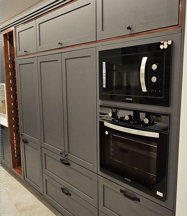 A união perfeita entre o design exclusivo e a paz de uma organização inteligente. Cozinha de alto padrão com armários escuros, detalhes em palhinha e torre de eletrodomésticos - Batel Select Curitiba.