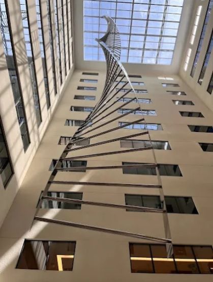 Átrio interno do Edifício DOC Batel, em Curitiba, com claraboia e escultura em espiral — acesso ao studio da Batel Select móveis planejados.