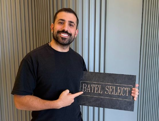 Kaysar Dadour sorrindo e apontando para placa com logo da Batel Select, especialista em móveis planejados para apartamentos pequenos em Curitiba.