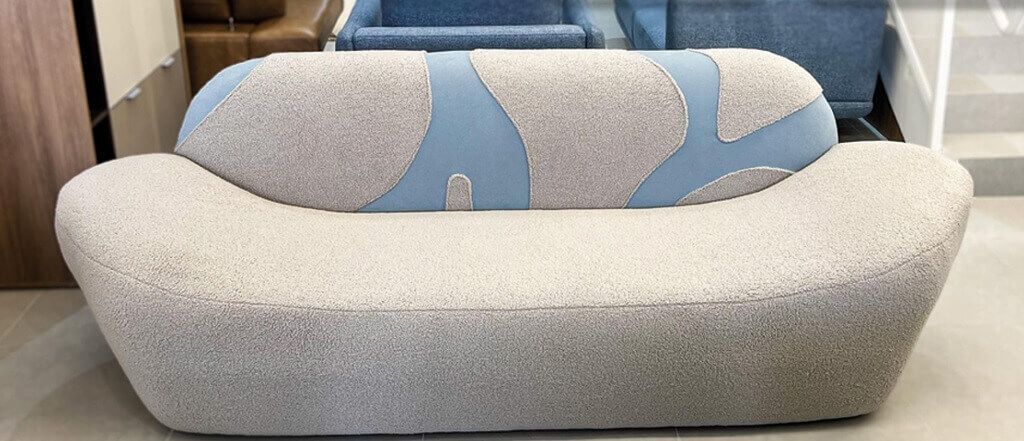 Sofá orgânico de alto padrão em Curitiba, com formato curvo, revestido em tecido bege claro, almofadas em tricô e design contemporâneo aconchegante.