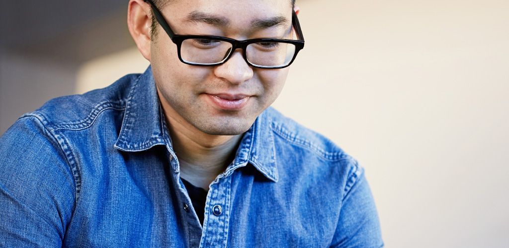 A man wearing glasses and a denim shirt is looking down.