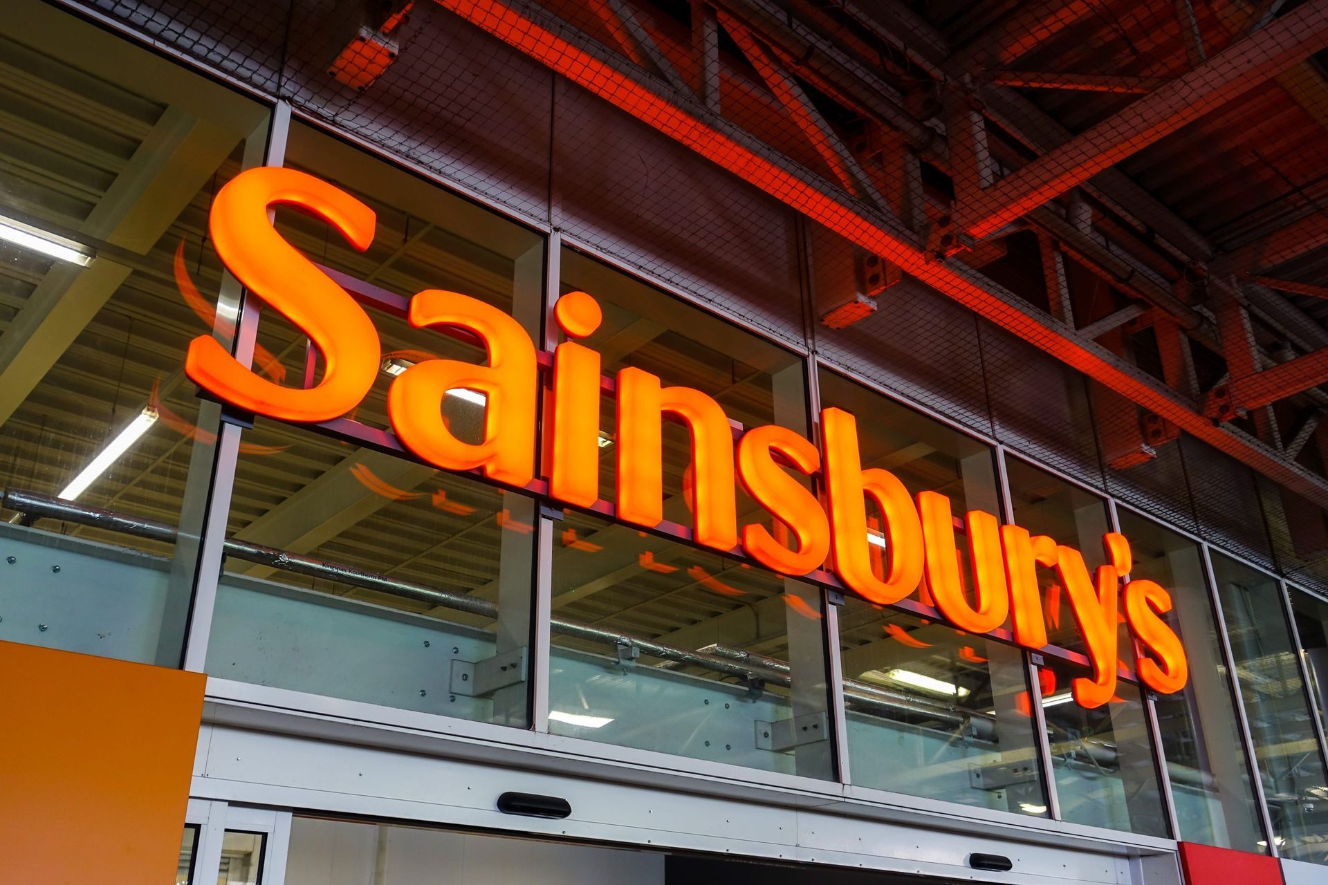 A sign for sainsbury 's is hanging from the ceiling of a store.