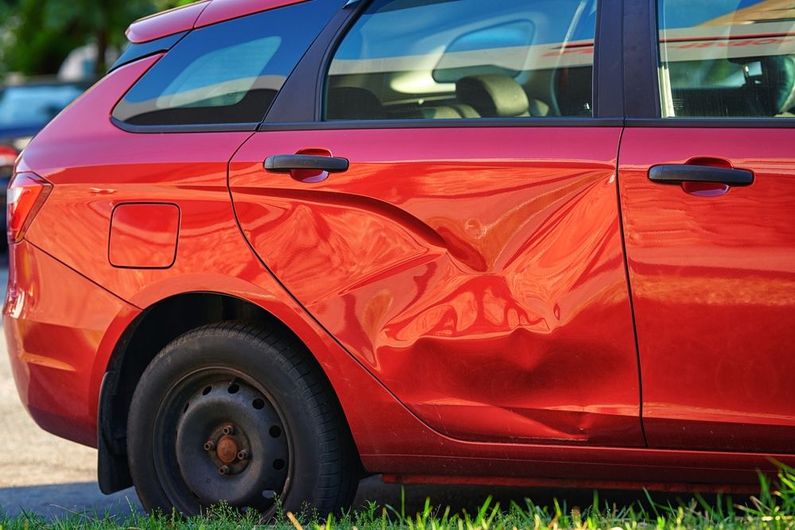 A red car with a large, deep dent on the rear passenger-side door.