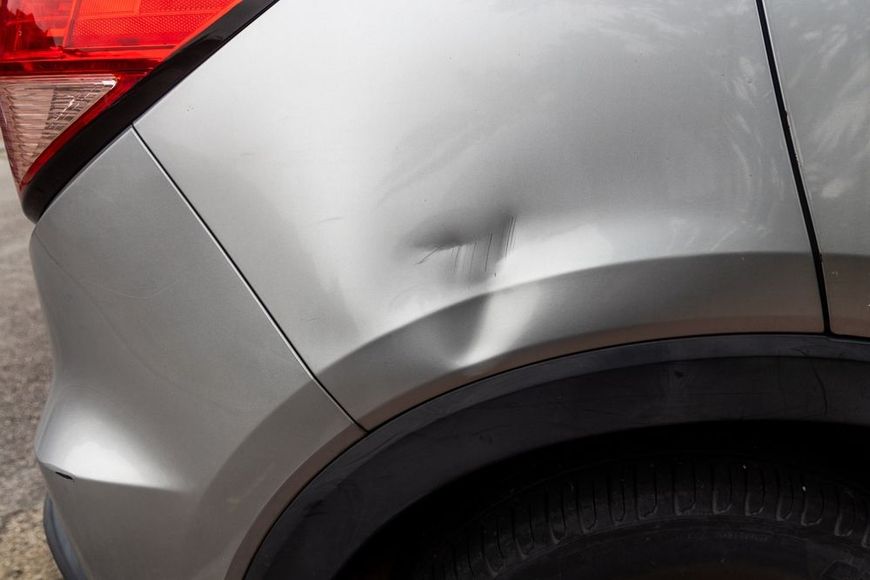A silver car's rear quarter panel shows a noticeable dent above the wheel well.
