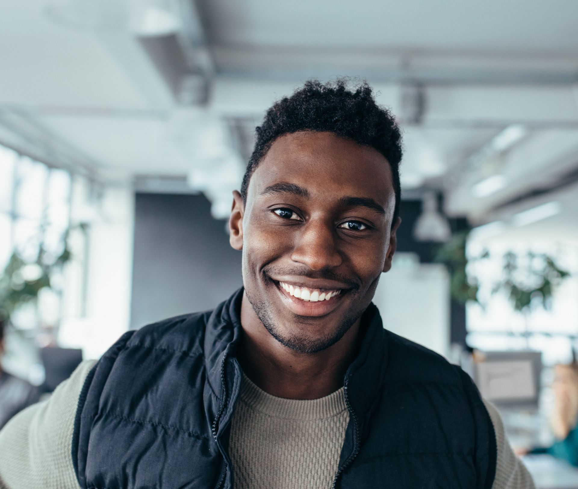 A man wearing a black vest and a sweater is smiling for the camera.