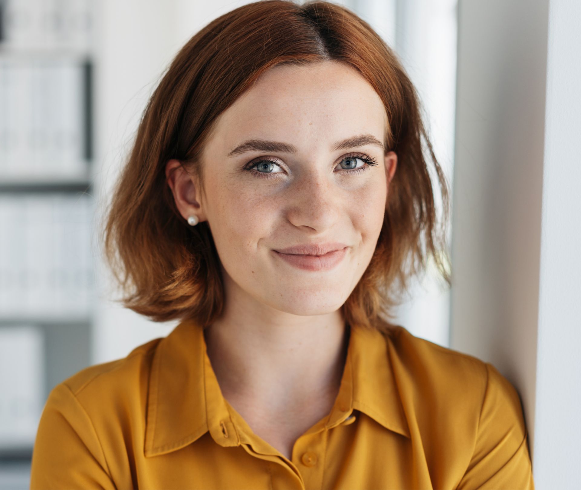 A woman in a yellow shirt is leaning against a wall and smiling.