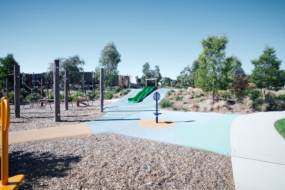 A sunny playground with a green slide, brown wood chip ground, and light blue rubber pathways — Quarrell Civil Construction In Echuca, VIC