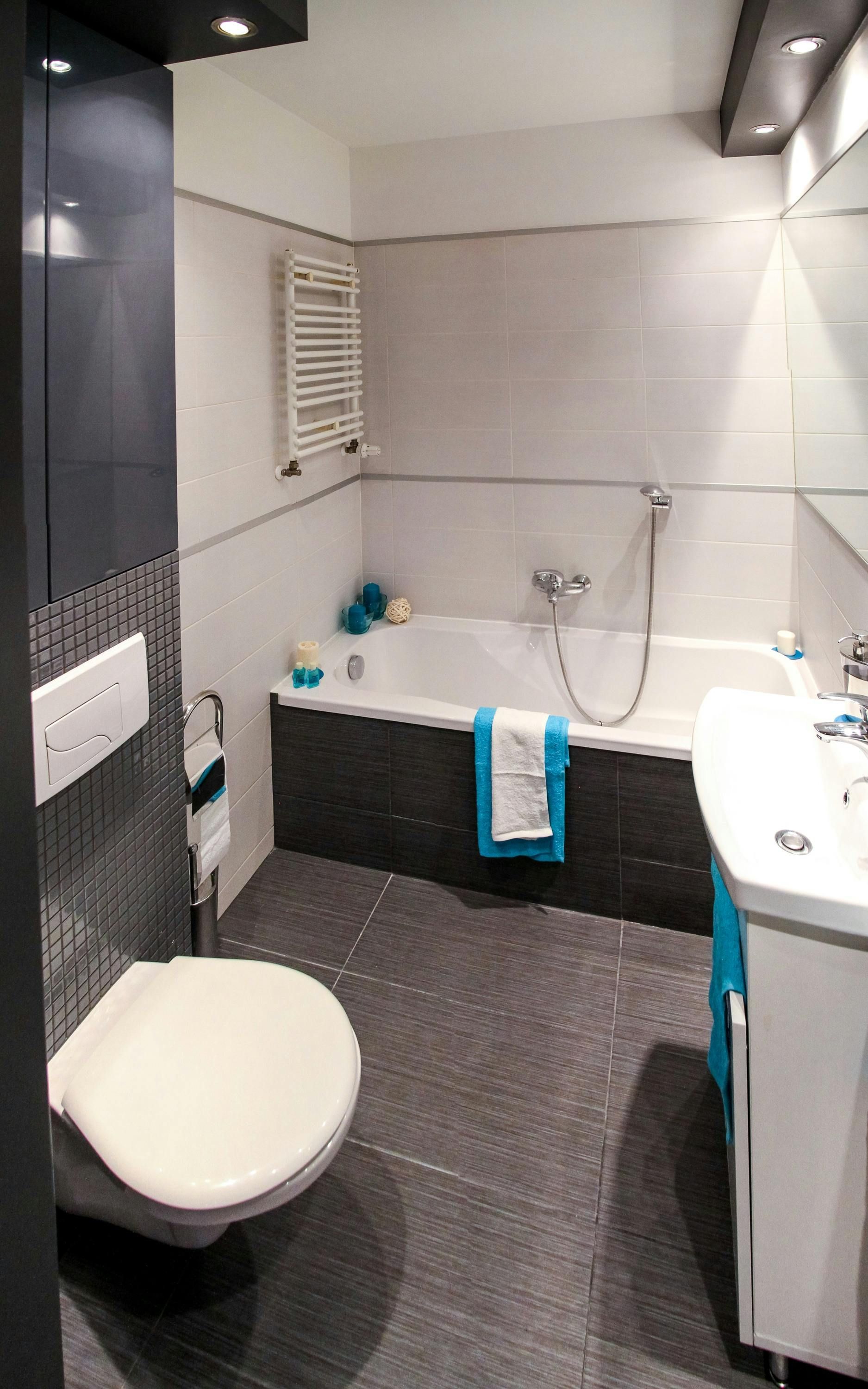 Modern bathroom with dark gray tile floor, white tub, and teal accents.